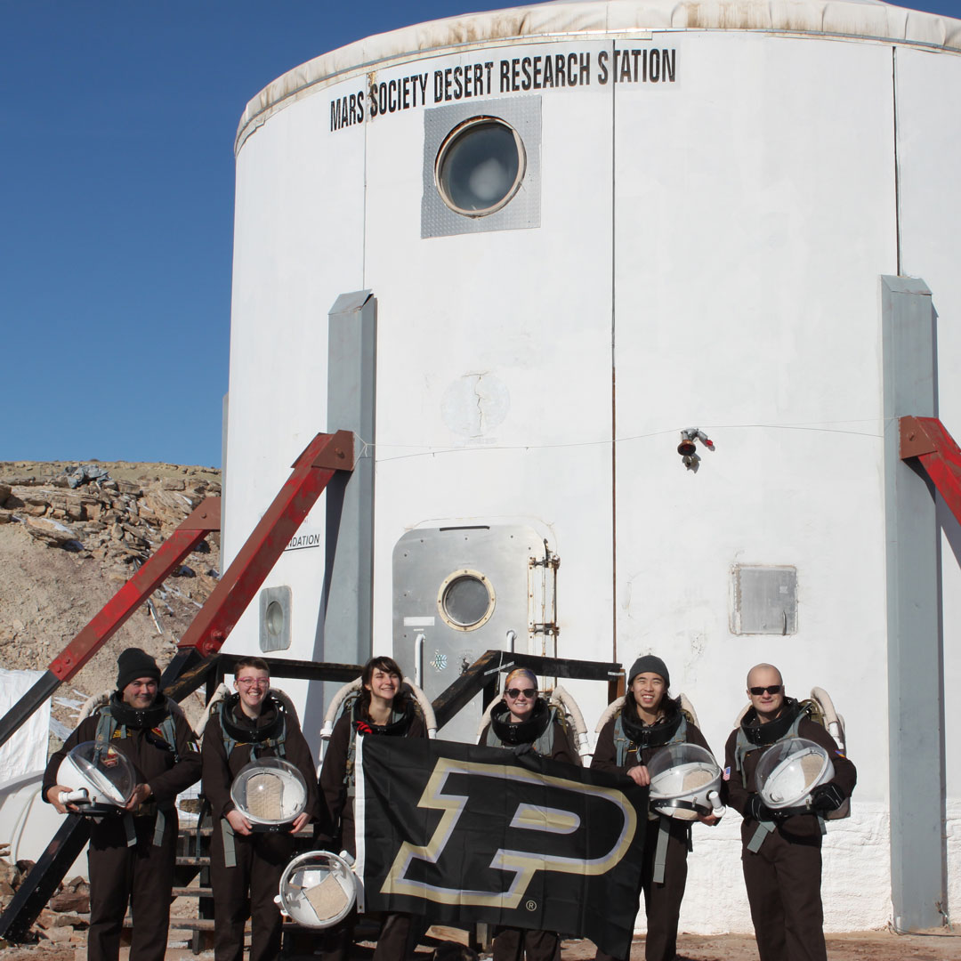 The Mars Society MDRS Crew 202 from Purdue University stands with the Purdue flag in front of their habitat for the next two weeks.