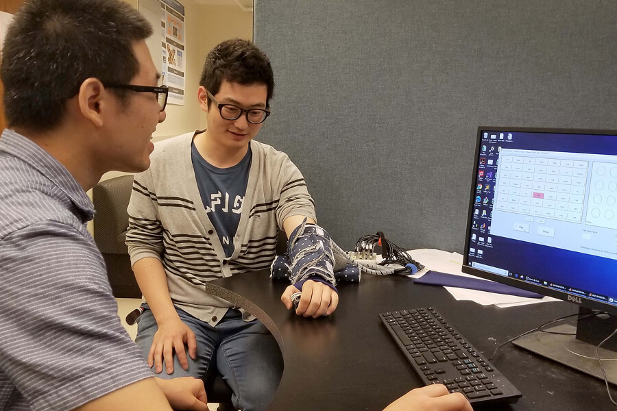 Postdoctoral student Yang Jiao communicates words to Jaeong Jung, an undergraduate student, using phoneme signals transmitted to the haptic device on his forearm.