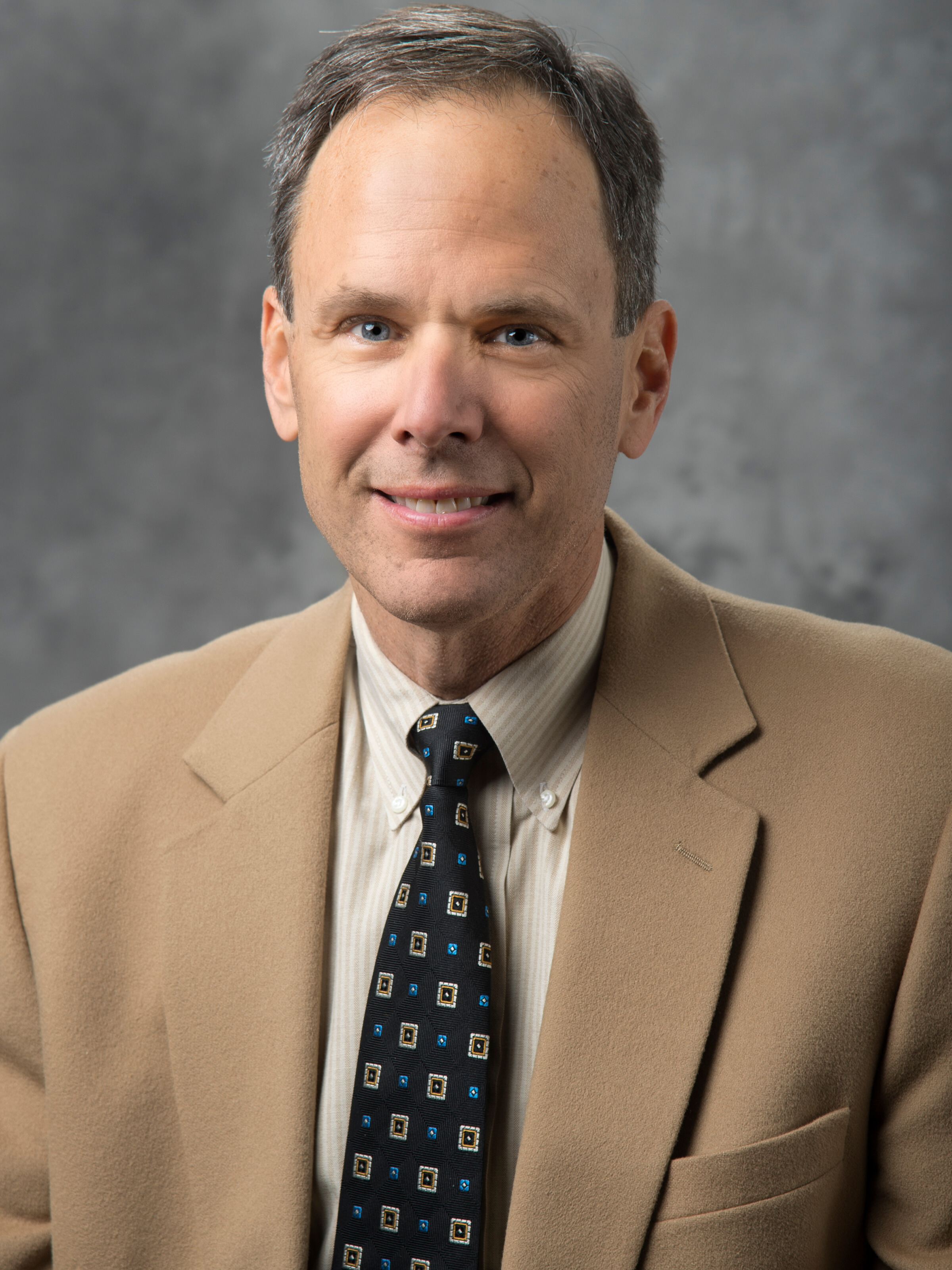 A portrait-style photo of Mark Gruninger with a gray background.