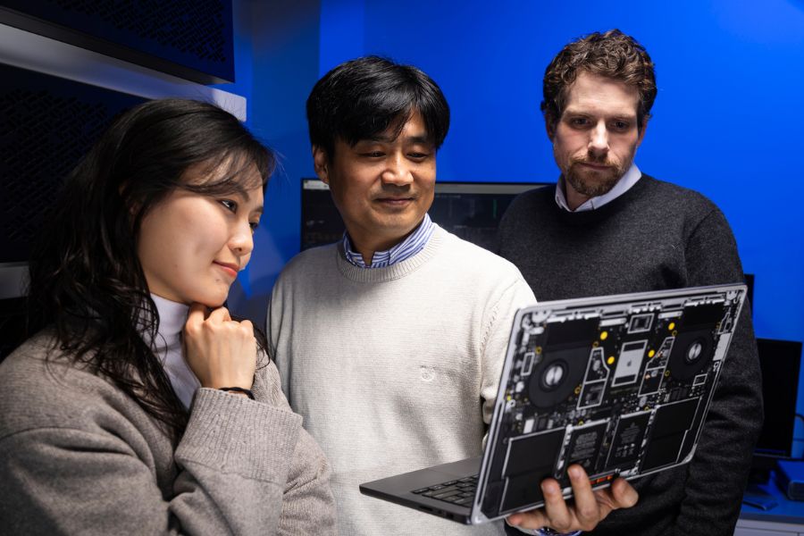 Researchers stand shoulder to shoulder while looking a laptop computer.