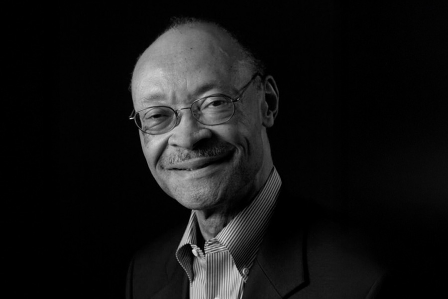 A black-and-white portrait of Frank Greene, wearing a striped button-up shirt and a blazer.