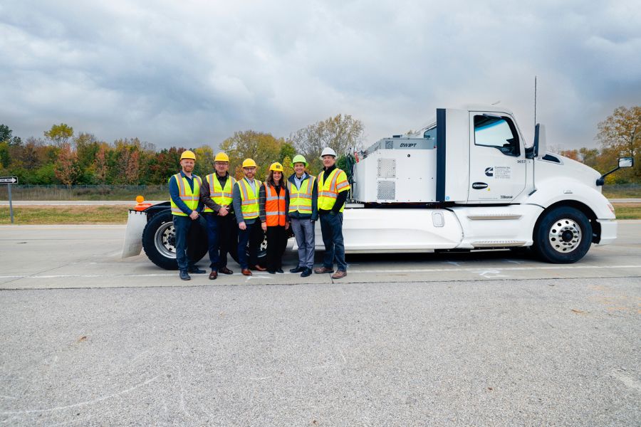 A group of researchers pose in front of a white semitruck while wearing bright yellow vests and hard hats.