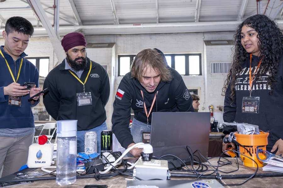 Four StarkHacks participants gather around a laptop and hardware components at a workstation inside the Purdue University Armory during the 36-hour hardware hackathon.