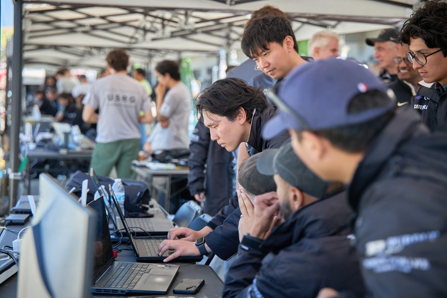 Purdue AI Racing team members review data on laptops in the pit area at Laguna Seca.