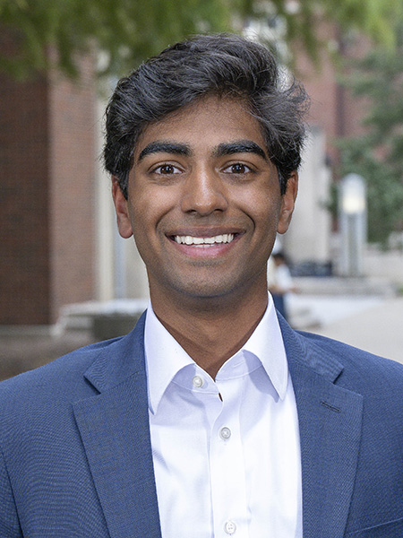 Student with short dark hair, brown eyes, smiling; wearing a navy jacket and white collared shirt