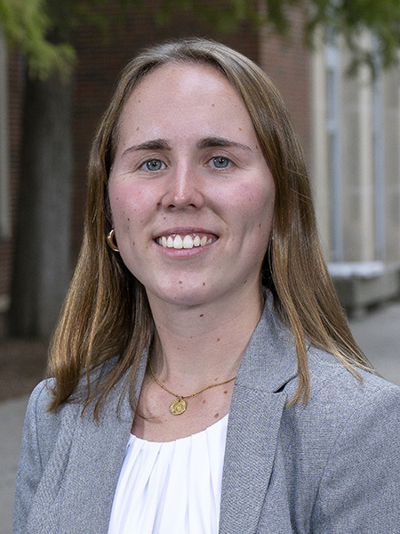Student with long hair and blue eyes wearing gold hoop earrings and gray jacket