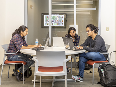 Three students working together in a small windowed conference room