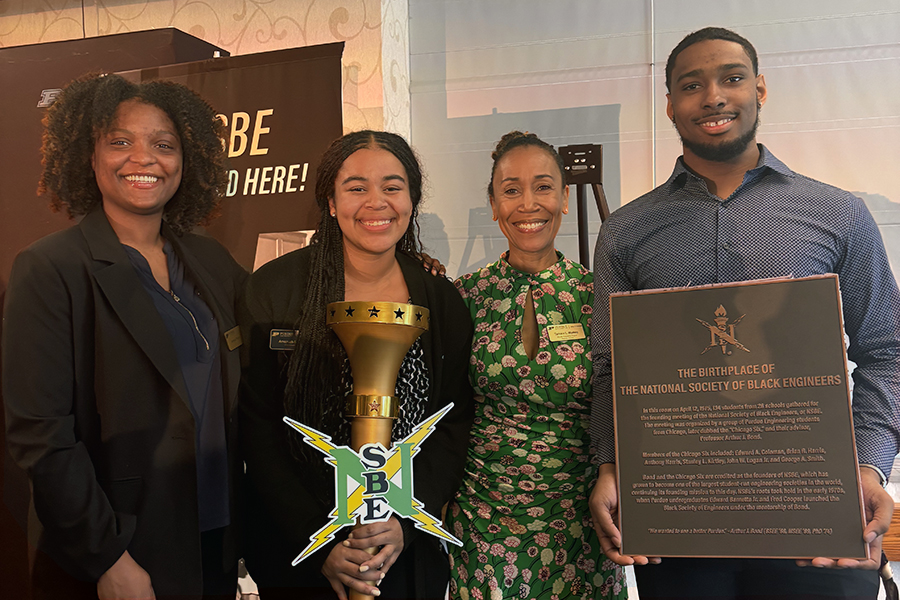 Four people smiling, one holding a plaque to celebrate NSBE's 50th anniversary