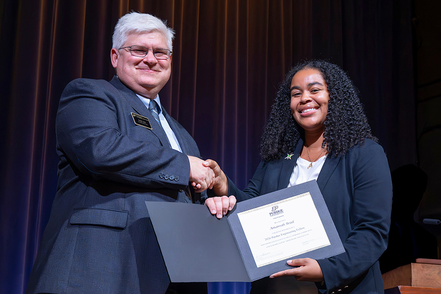 Man with gray hair and glasses smiling, shaking hands with student, hold a certificate for Purdue Engineering Fellows