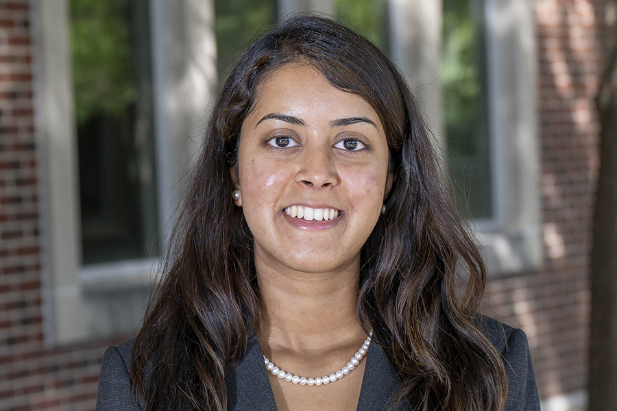 Student with long, brown hair, smiling, wearing pearls and a blue jacket