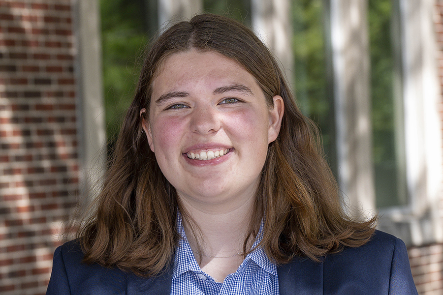 Photo of a woman with dark brown hair, smiling wearing a blue checkered shirt and navy blazer