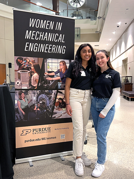 Pandya with another student earing black polo shirts, standing in front of banner that reads "mechanical engineering"