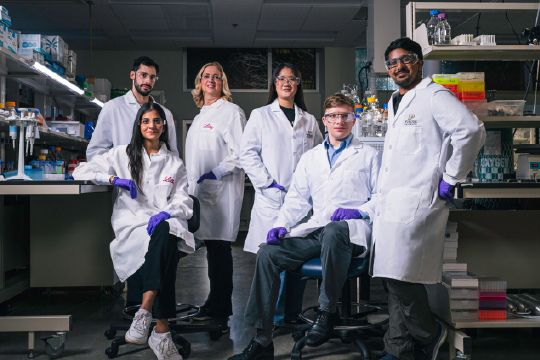 Purdue researchers and Eli Lilly and Company scientists photographed in lab setting wearing lab coats and safety glasses.