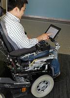 Alexander Lo, a researcher in the Purdue Center for Paralysis Research, uses an iPad on the RoboDesk.  (Purdue Research Foundation Photo)