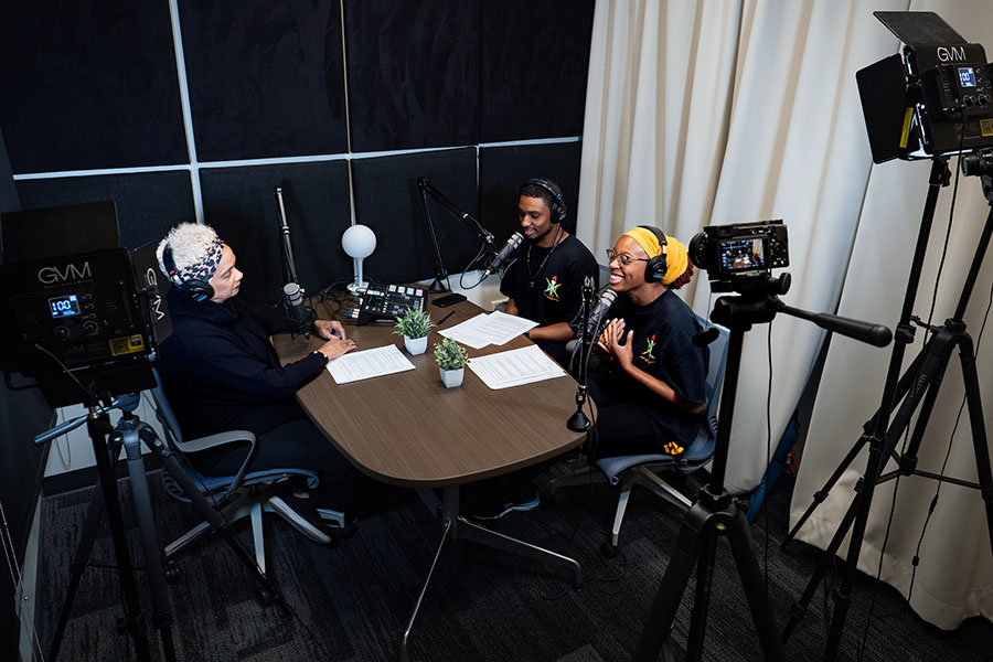 Behind the scenes of the recording of the podcast, three people inside the studio wearing headphones and sitting at a table