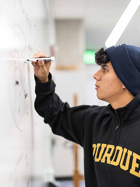 Oliver Juarez, wearing a beanie, writes on a dry erase board in the ASC