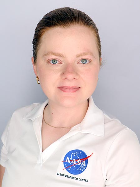Woman with blue eyes and red hair (pulled back in ponytail) wearing white polo shirt