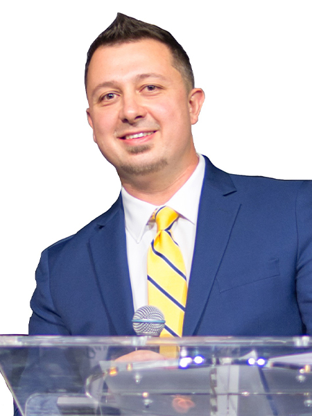 Portrait of a man in a blue suit and yellow tie with a microphone.