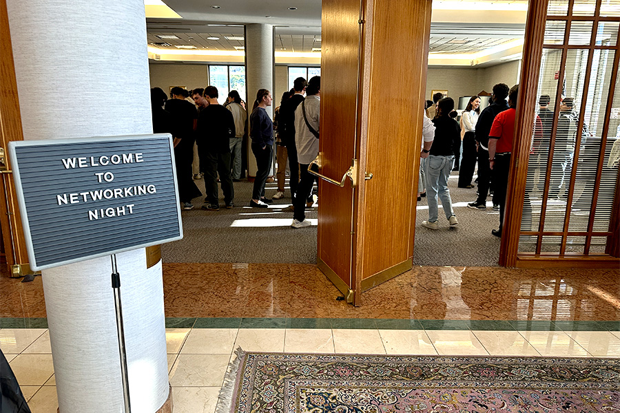 Brown doors with people standing in the background. Sign in foreground reads, "Welcome to Networking Night."