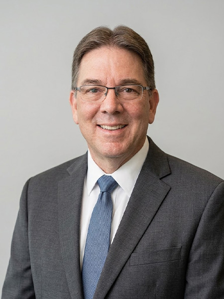 Man with brown hair and glasses, in a gray suit and blue tie.