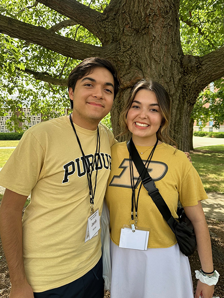 Brother and sister on campus together in front of a tree.
