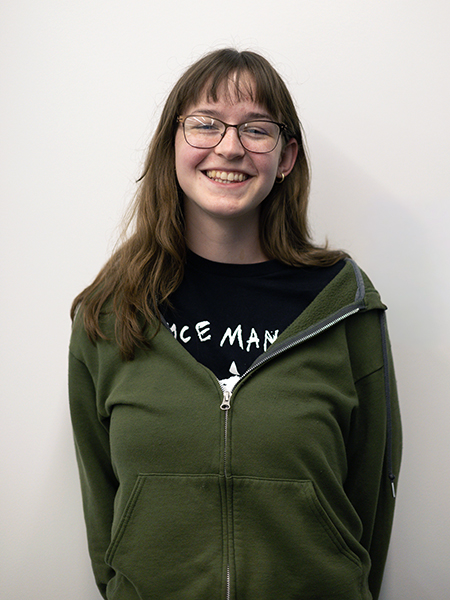 Student wearing a green zip-up sweatshirt, glasses, dark hair with bangs