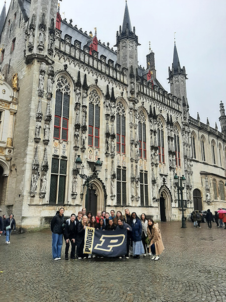group of women posing in front of building holding a Purdue flag
