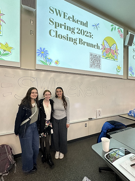 Three students in a classroom, standing in front of a whiteboard with "SWEekend" written on it