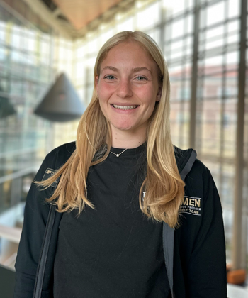Student with long blonde hair, smiling, wearing black pullover with "Women in Engineering Program" on the chest