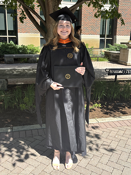 Student with long blonde hair wearing black cap and gown, holding diploma