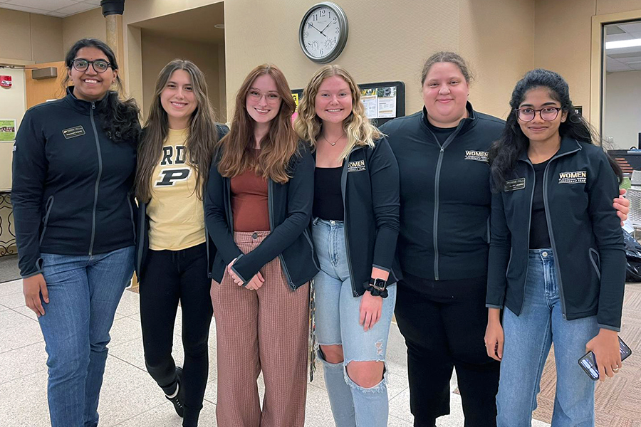 Six women smiling, wearing matching black Women in Engineering Program zip-up jackets