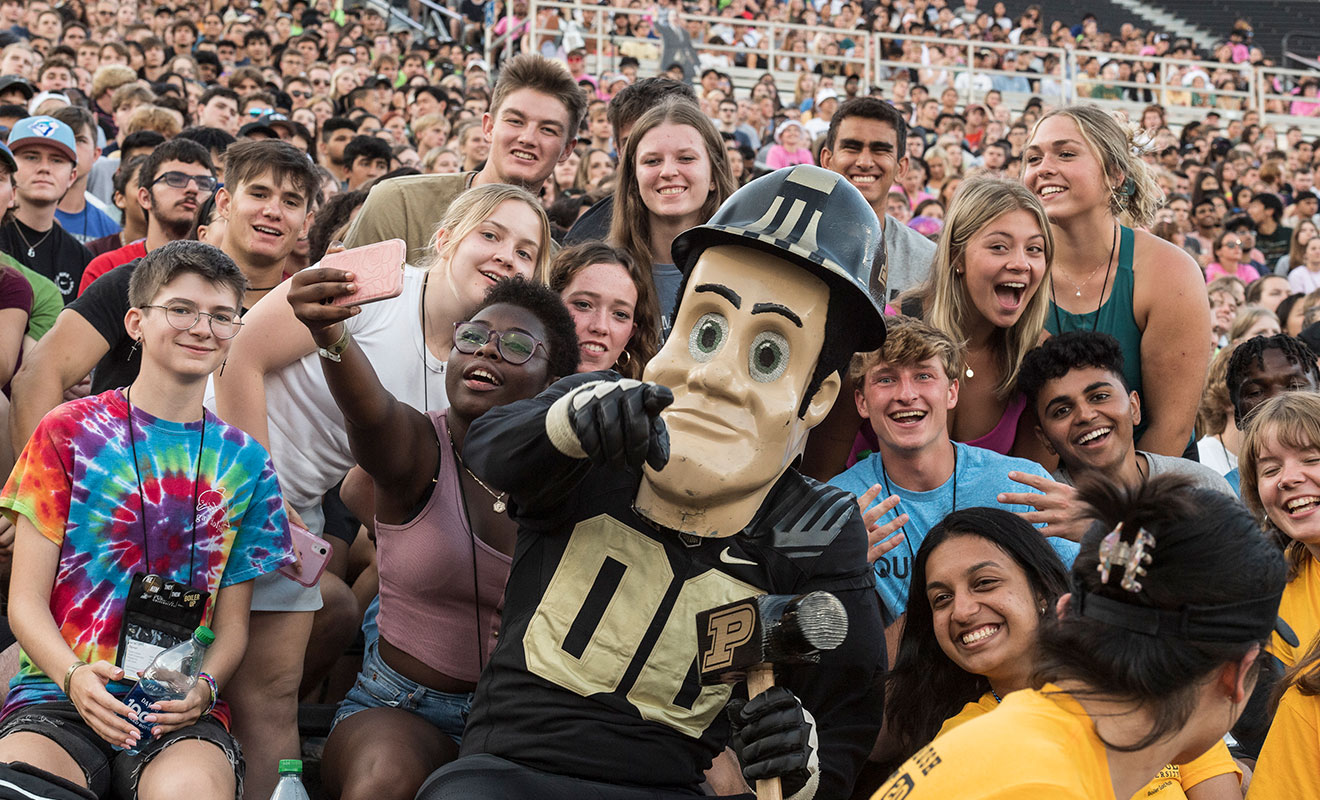 Purdue Pete and students posing for photo at a Purdue game at the stadium. Lots of happy faces.