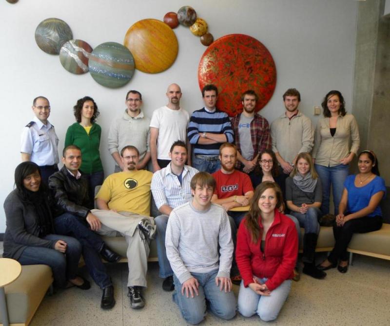The research group among the planetary display, December 2012. Back row: Chris Geisel, Lucia Capdevila, Loic Chappaz, Jeff Stuart, Davide Guzzetti, Ted Wahl, Galen Harden, and Mar Vaquero. Middle row: Bonnie Prado Pino, Rohan Sood, Cody Short, Wayne Schlei, Chris Spreen, Tash Bosanac, Amanda Knutson, and Ash Das. Front row: Tom Pavlak and Amanda Haapala.