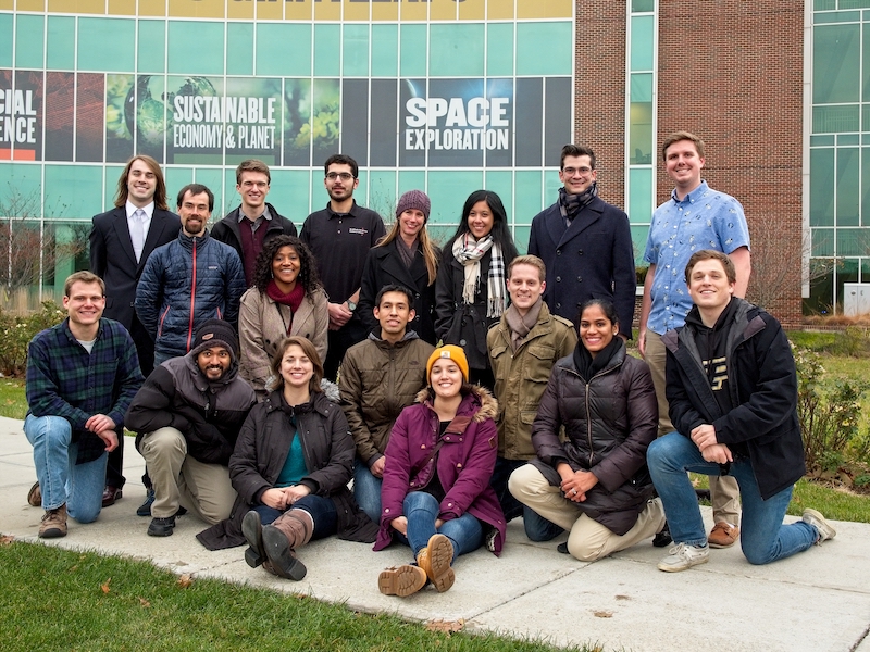 Prof. Howell's research group in front of a banner celebrating Purdue's contributions to space exploration. Pictured: Robert Pritchett, Brian McCarthy, Andrew Cox, Vivek Muralidharan, Stephen Scheuerle, Bonnie Prado Pino, Emily Zimovan, Fouad Khoury, Juan Ojeda Romero, Diane Craig-Davis (alumni), Kenza Boudad, Maaninee Gupta, Matt Bolliger, David Canales, Ash Das-Stuart, Collin York, RJ Power.