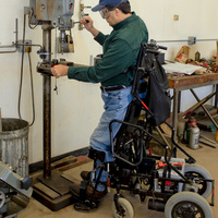 Paraplegic farmer in a standing wheelchair operates a drill press
