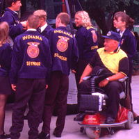 Paraplegic farmer sitting on a motorized wheelchair observes FFA students learning about assistive technology