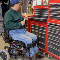 Paraplegic farmer rummages through his toolbench from a wheelchair