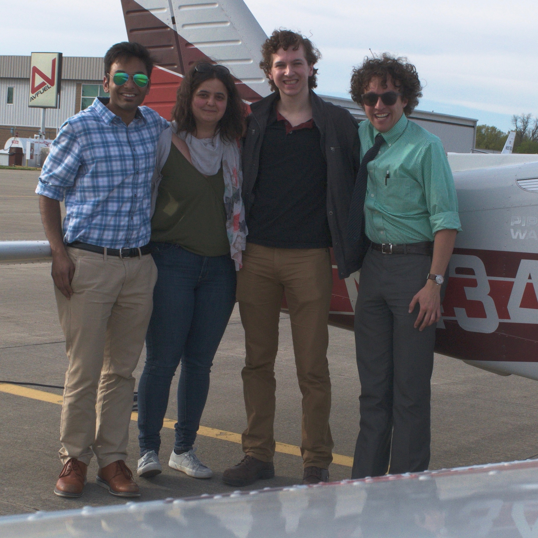 Four graduate studies standing next to a small airplane